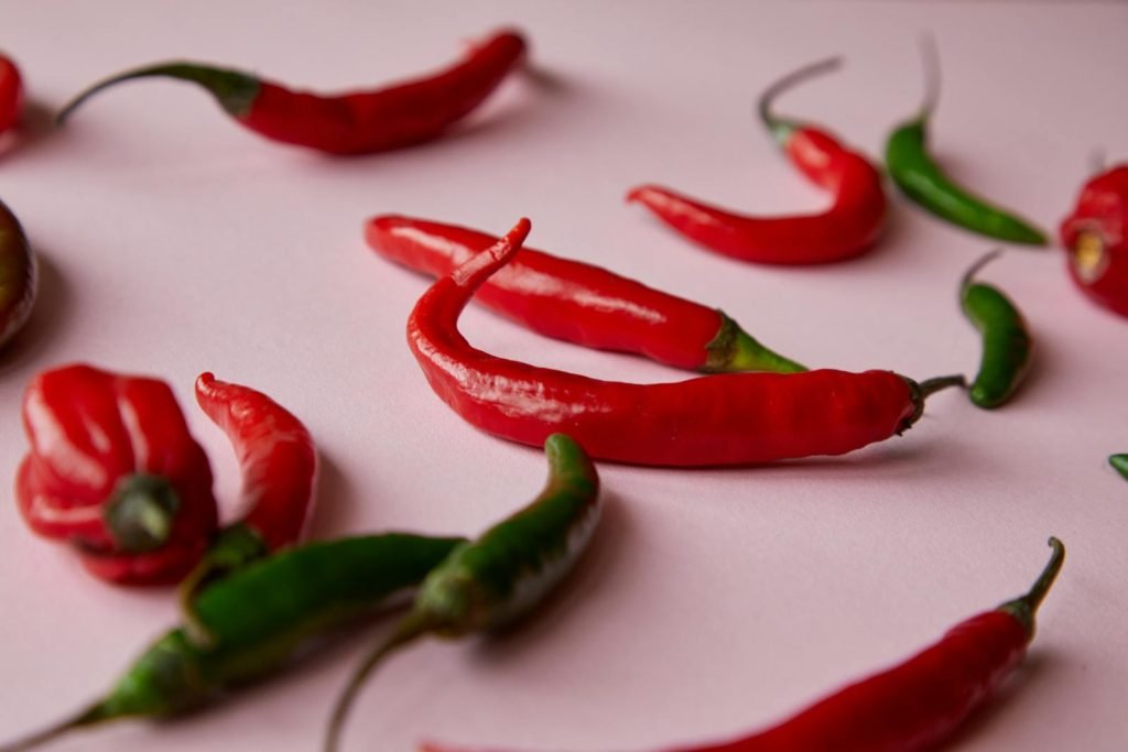 Ripe various red and green spicy chili peppers placed on pink surface in light place